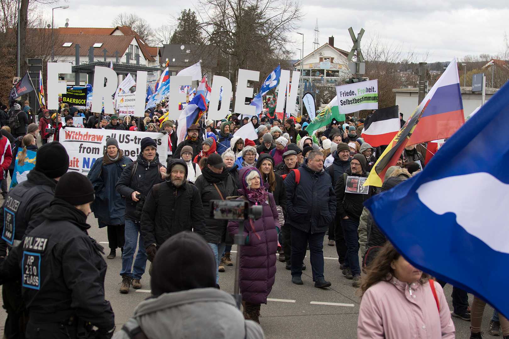 Foto der Demonstration in Ramstein. Im Hintergrund sind Buchstaben zu sehen, die jeweils von Teilnehmenden getragen werden und das Wort "Frieden" ergeben.